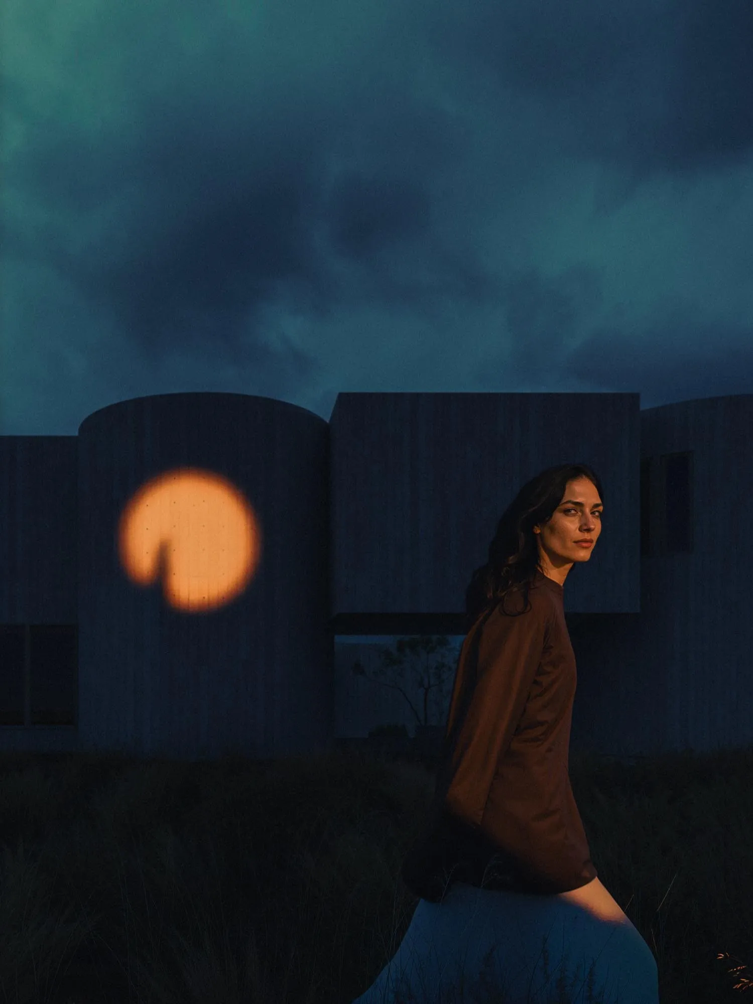 A woman by the round window at dusk