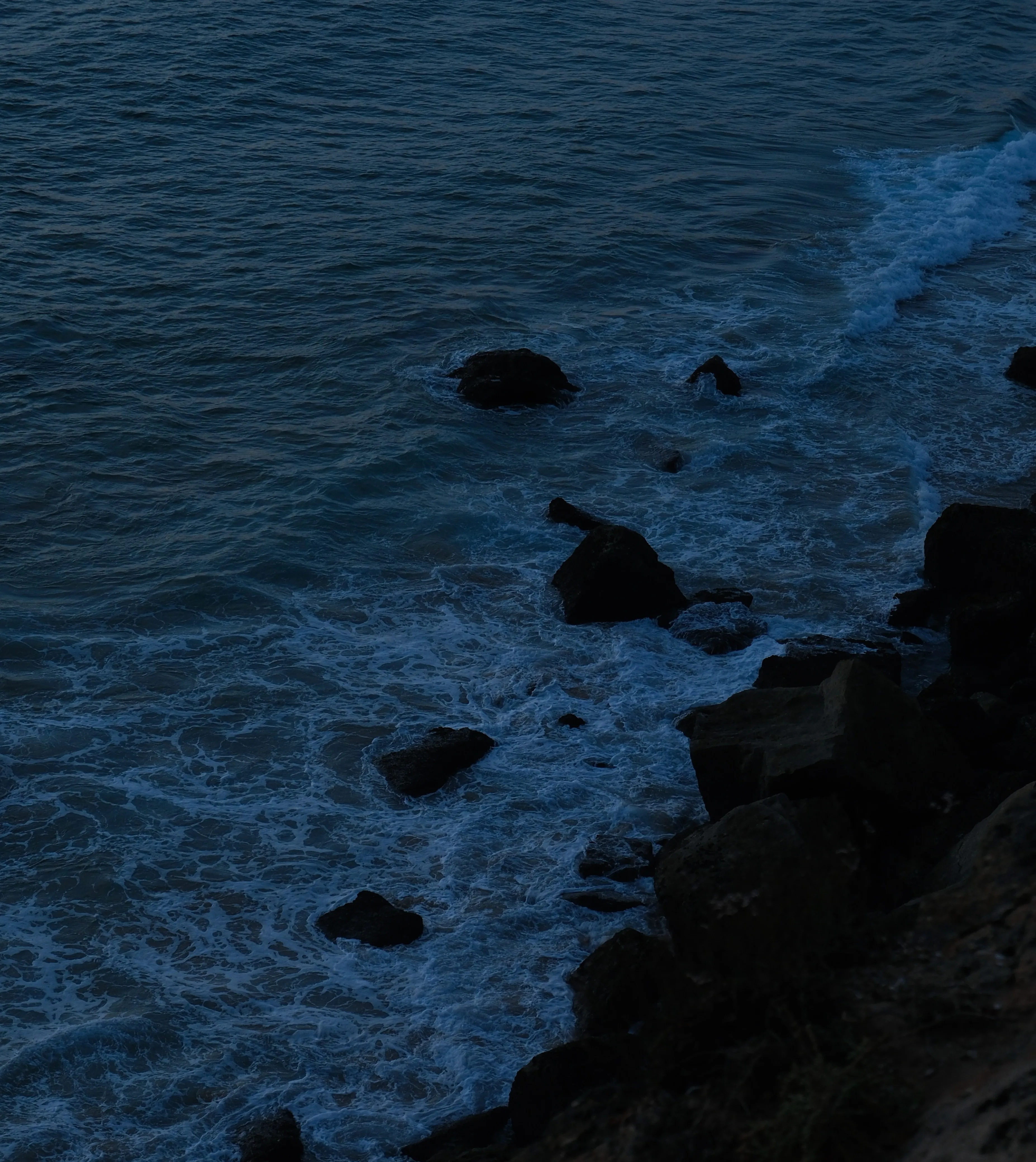 Waves breaking on dark rocks at dusk
