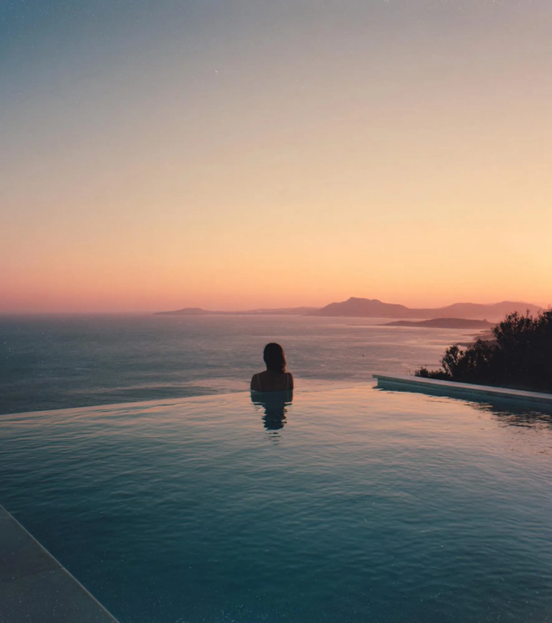 A figure in the infinity pool at sunset, the sea