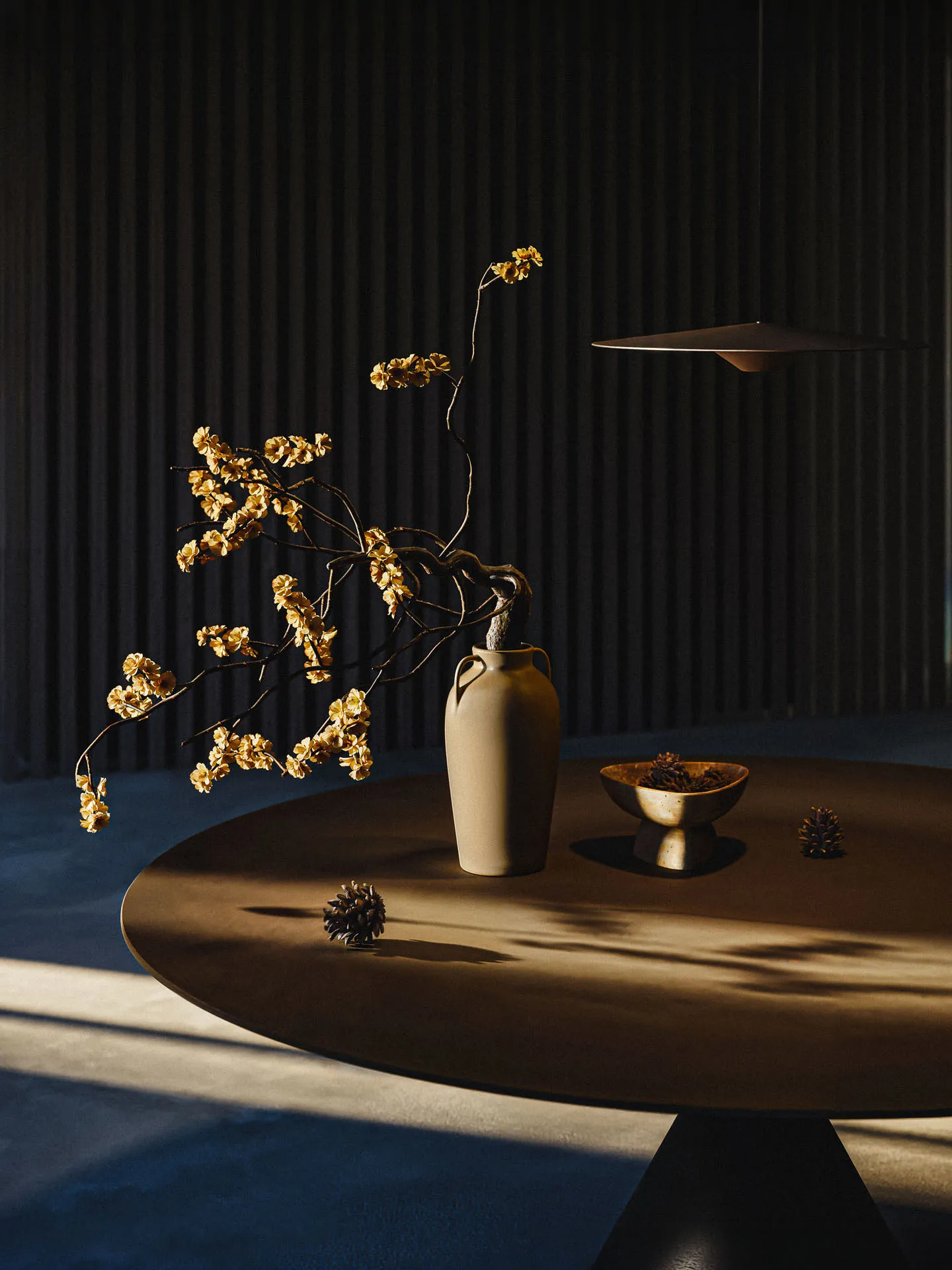Round wooden table with a vase of dried flowers against dark slats